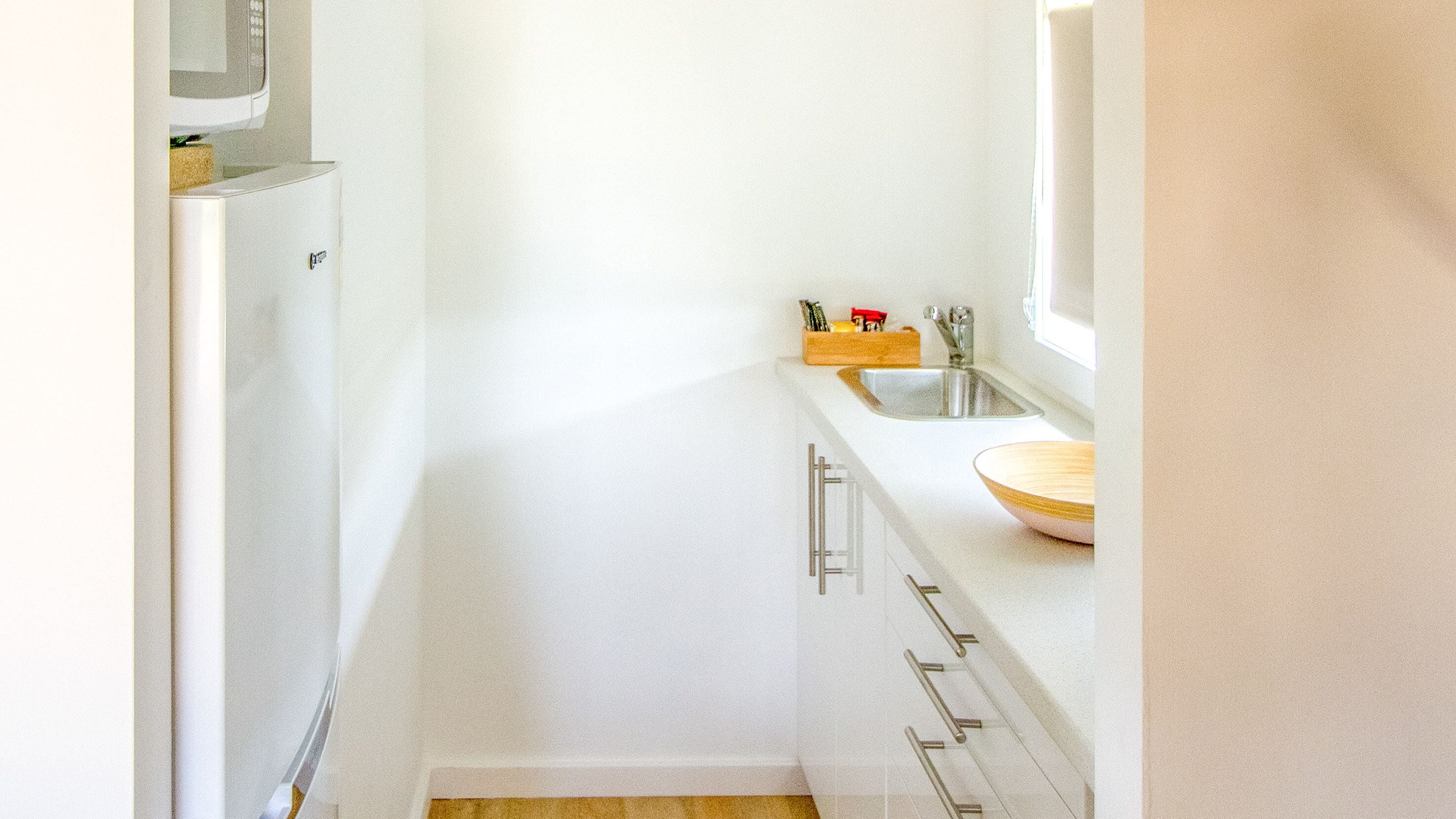 A narrow kitchen with white cabinets, a microwave, a sink, and a wooden bowl on the counter.