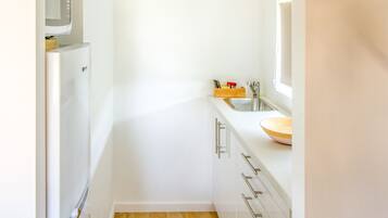 A narrow kitchen with white cabinets, a microwave, a sink, and a wooden bowl on the counter.