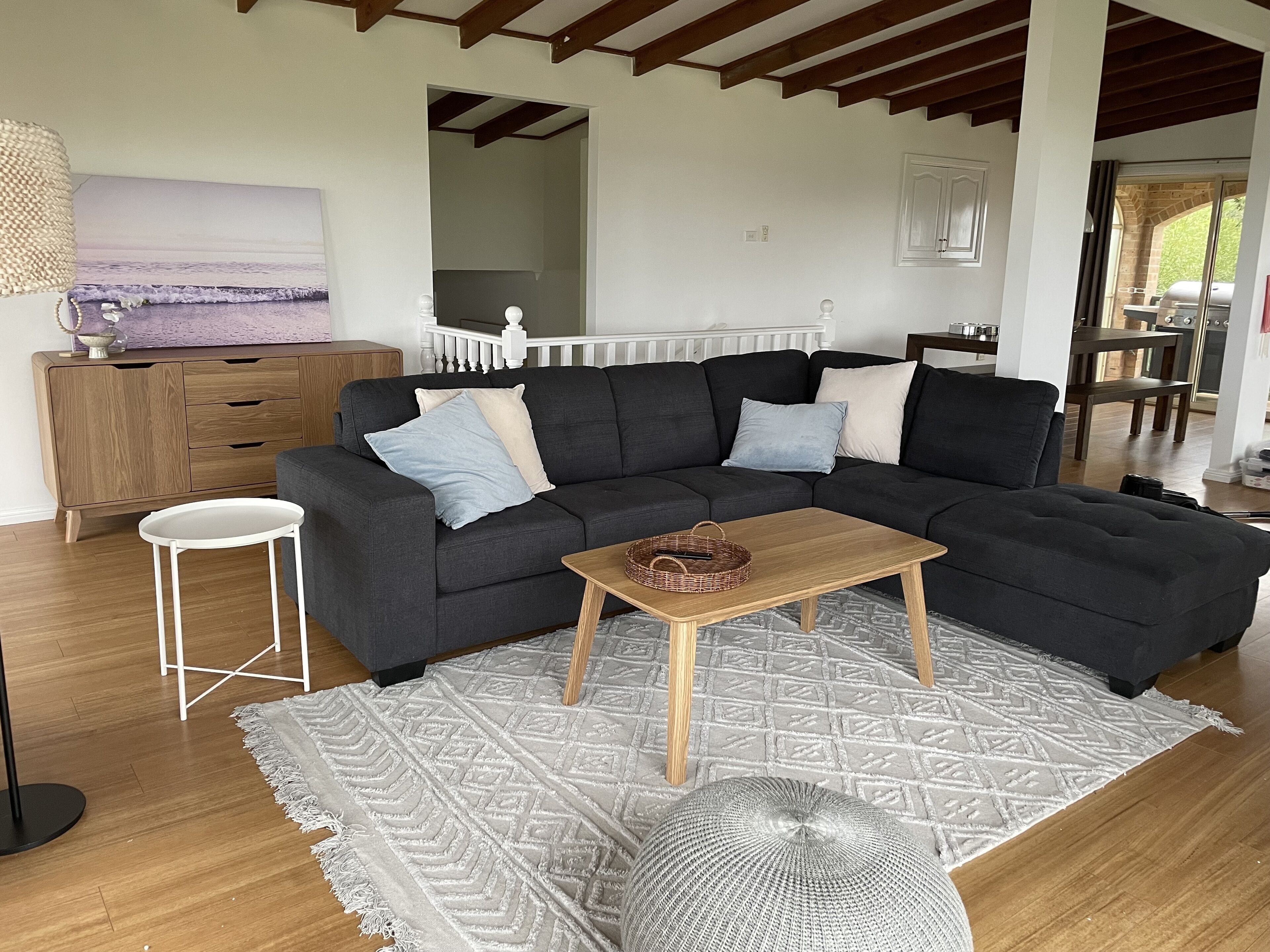 Un salon moderne avec un canapé d’angle, une petite table en bois et un tapis à motifs.
