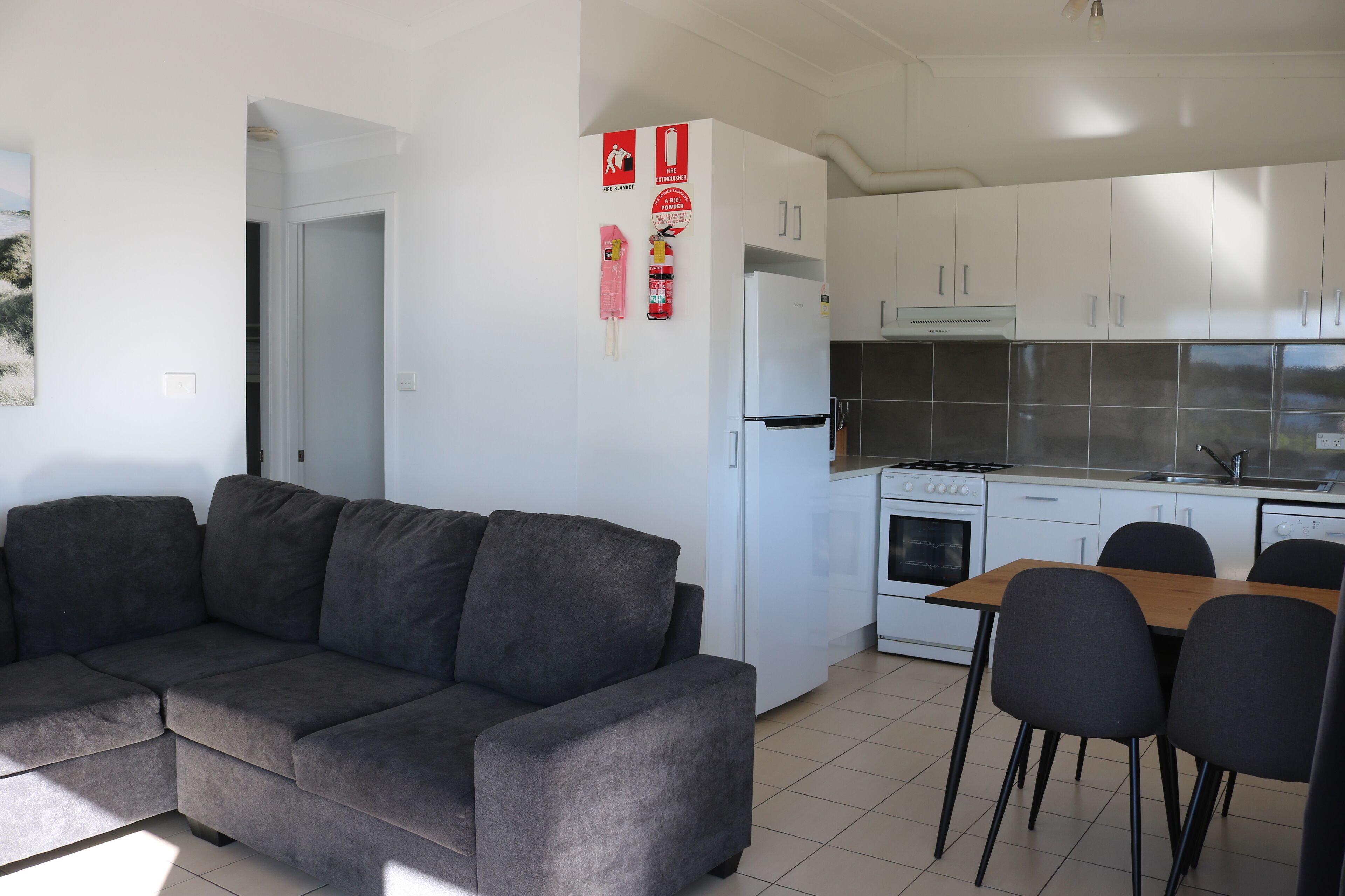 Una cocina moderna con armarios blancos, horno integrado y comedor con mesa de madera y cuatro sillas.