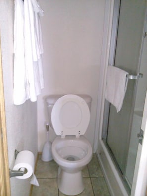 A small bathroom with a toilet, a shower, and a toilet paper holder. - Crystal Isles RV Resort (Crystal River)