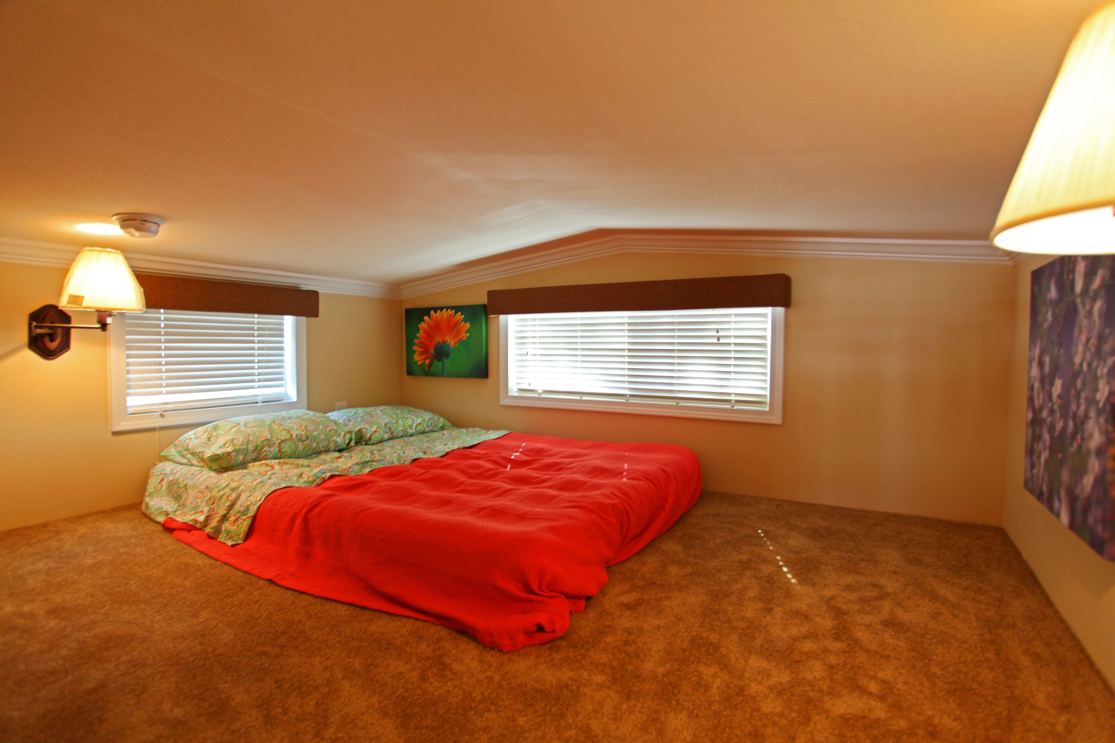 A bedroom with a single bed, two windows with blinds, a wall-mounted lamp, and a painting.
