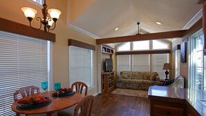 A dining area with a wooden table and chairs, a chandelier, and a television in the background.