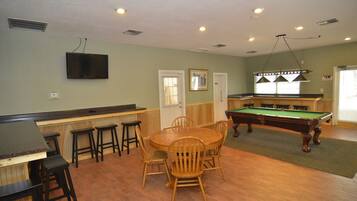 A pool table, bar area, and seating with a television above the bar.