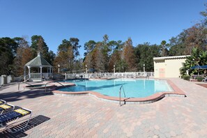Una piscina con un quiosco, sillones de descanso y una zona vallada.