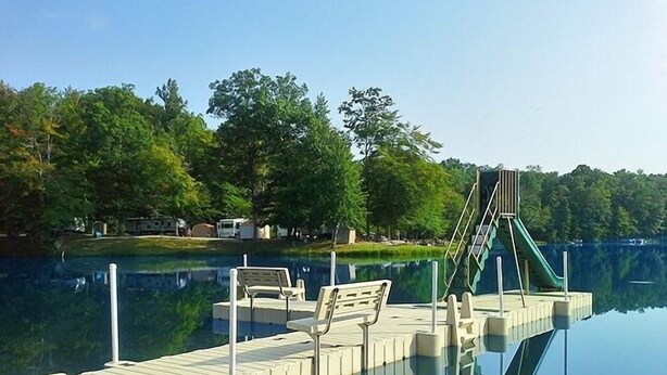 A calm lake with a dock extending into the water, featuring benches and a small staircase leading to a platform. - Indian Lakes RV Campground (Sunman)