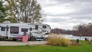 A white RV with a "Crown" logo parked near a lake, an American flag, and a picnic table. - Indian Lakes RV Campground (Sunman)
