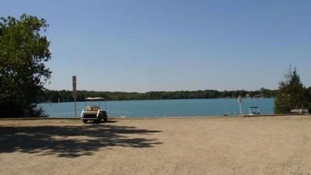 Une plage de sable avec un véhicule garé et une étendue d’eau en arrière-plan.