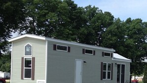 Une maison mobile de plain-pied avec une véranda, un petit garage attenant et une table de pique-nique.
