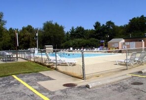 A fenced swimming pool area with lounge chairs and a small building in the background.