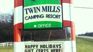 Une enseigne pour le camping Twin Mills, aux couleurs vert et blanc, avec une illustration de moulin à vent et une flèche indiquant la direction des bureaux.