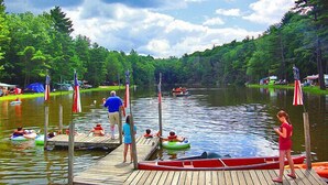 A wooden dock with people on boats and rafts, surrounded by trees and a calm lake. - Sturbridge RV Resort - Campground (Sturbridge)