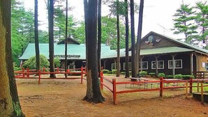 A rustic lodge with a green roof, surrounded by tall trees and a red wooden fence. - Sturbridge RV Resort - Campground (Sturbridge)