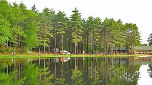 A serene lakeside view with tall trees and a building in the background. - Sturbridge RV Resort - Campground (Sturbridge)