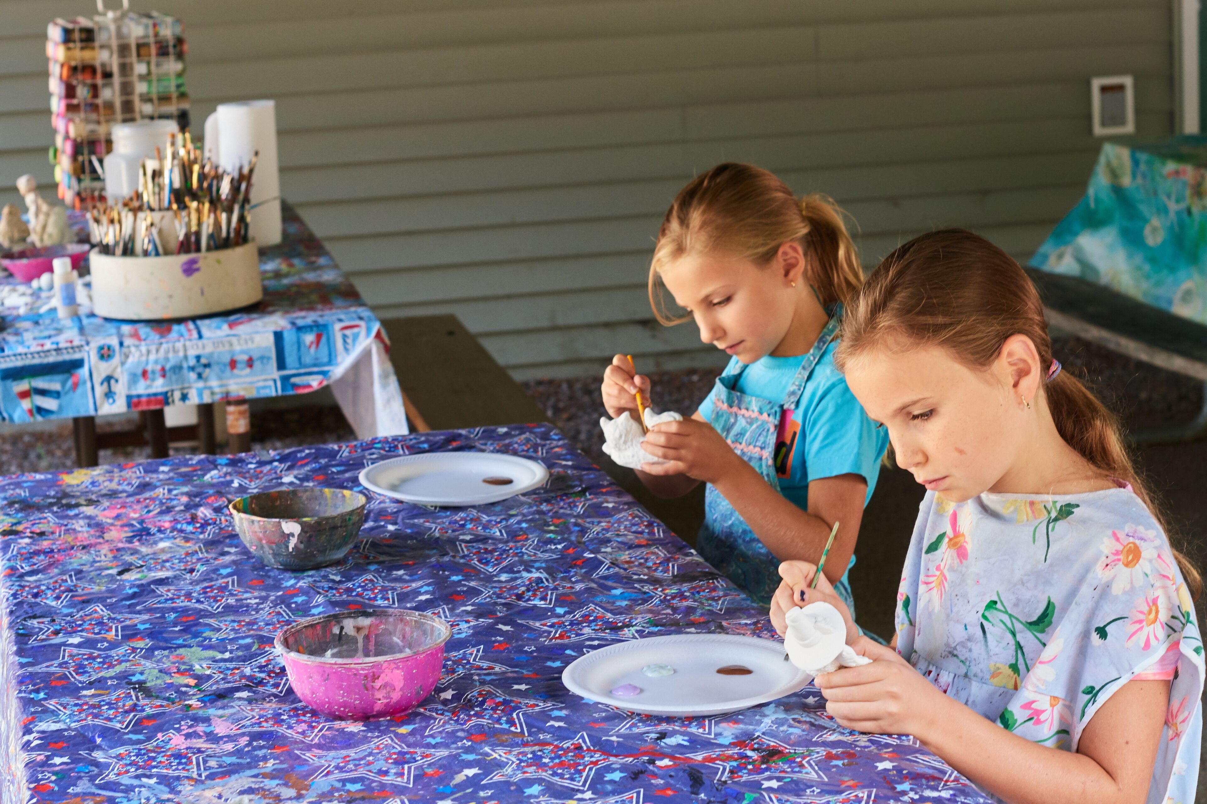 A table with a colorful tablecloth, bowls, and paintbrushes.