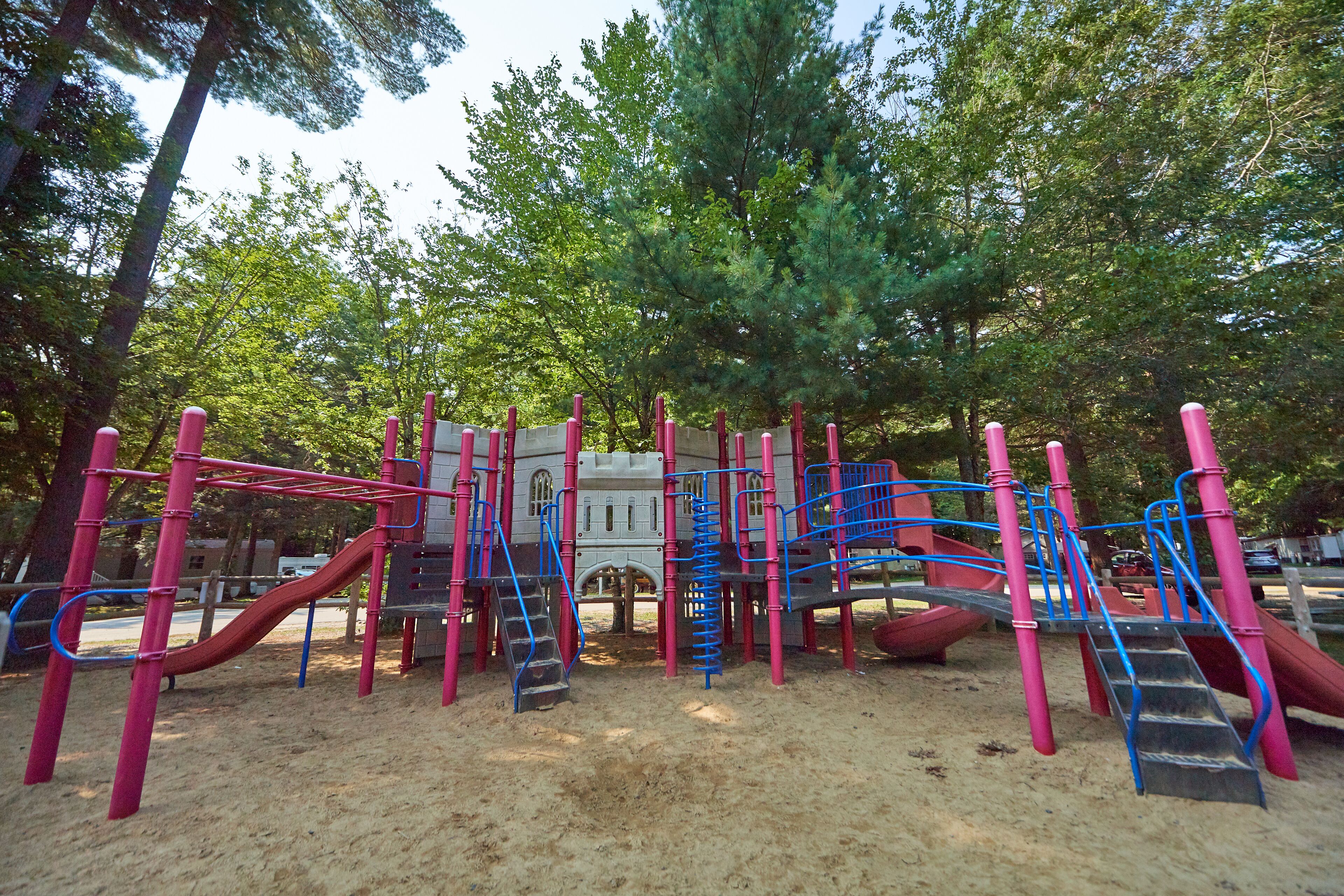 A playground with multiple slides and climbing structures, surrounded by trees.