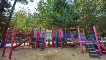A playground with multiple slides and climbing structures, surrounded by trees.