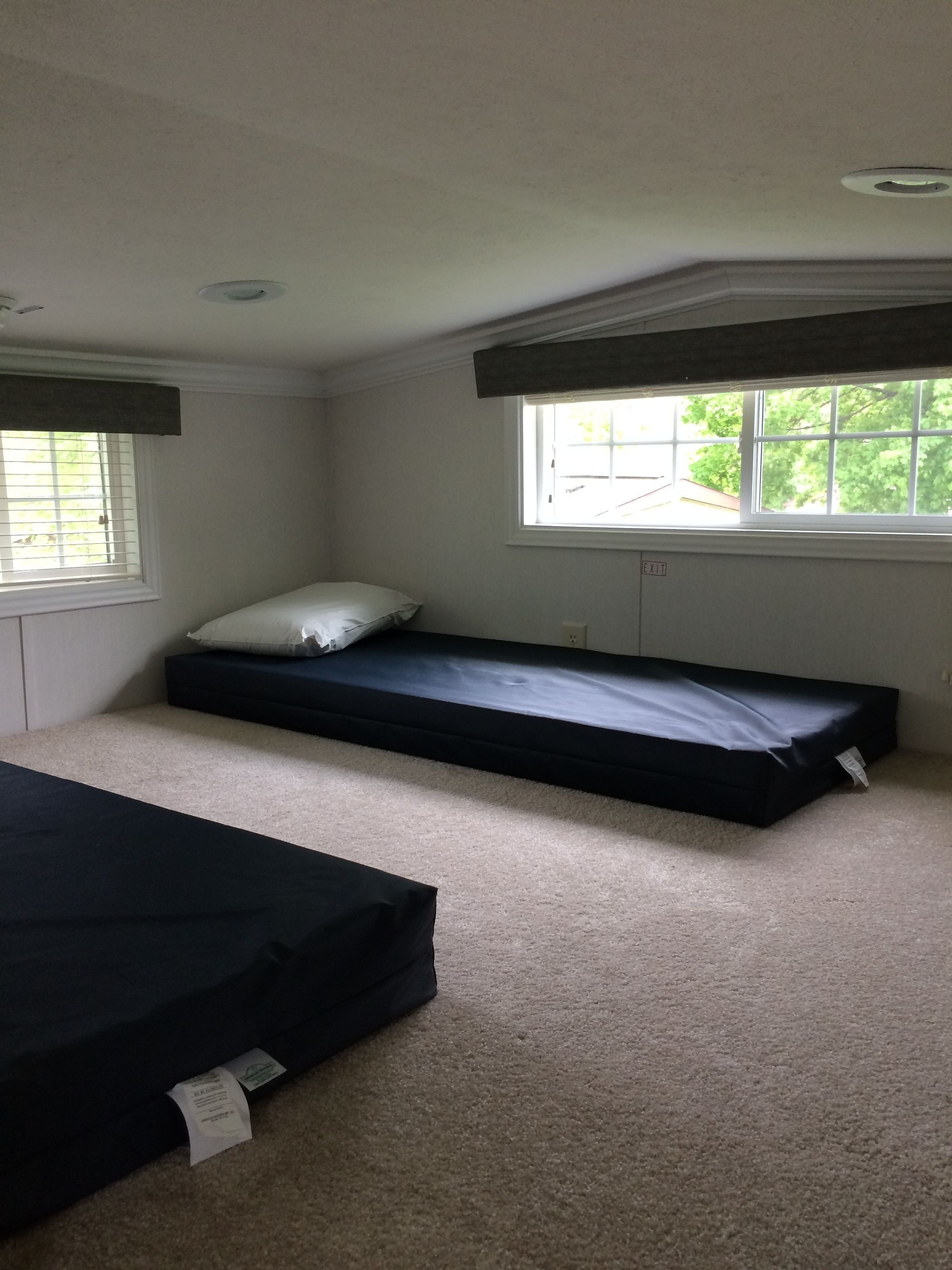 A small, carpeted room with two single beds, a window, and a ceiling vent.