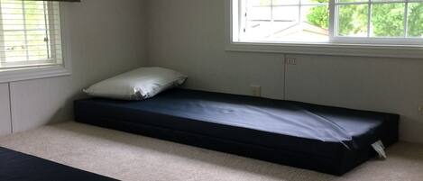 A small, carpeted room with two single beds, a window, and a ceiling vent.