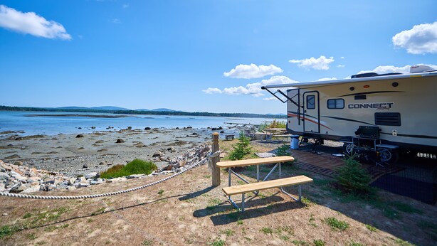 A recreational vehicle (RV) named 'CONNECT' parked by a lakeside with picnic tables and a rope barrier. - Narrows Too Camping Resort (Trenton)