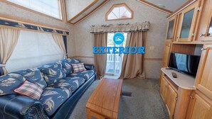 A cozy RV interior with a sofa, a wooden table, and a TV on a cabinet. - Narrows Too Camping Resort (Trenton)