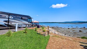 A recreational vehicle parked near a beach with a clear view of the water and distant hills. - Narrows Too Camping Resort (Trenton)