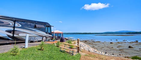 Una autocaravana estacionada cerca de una playa con vista despejada al agua y colinas lejanas.