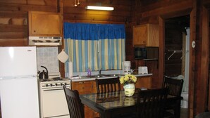 A wooden cabin-style kitchen with a stove, sink, and dining table with chairs. - Forest Lake RV & Camping Resort (Advance)
