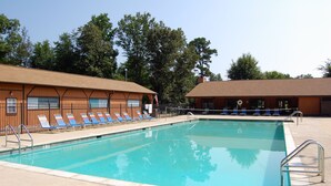 A swimming pool with lounge chairs and a building with a brick facade. - Forest Lake RV & Camping Resort (Advance)