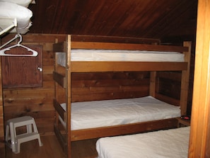 Quarto com beliches, paredes de madeira e um banquinho pequeno.