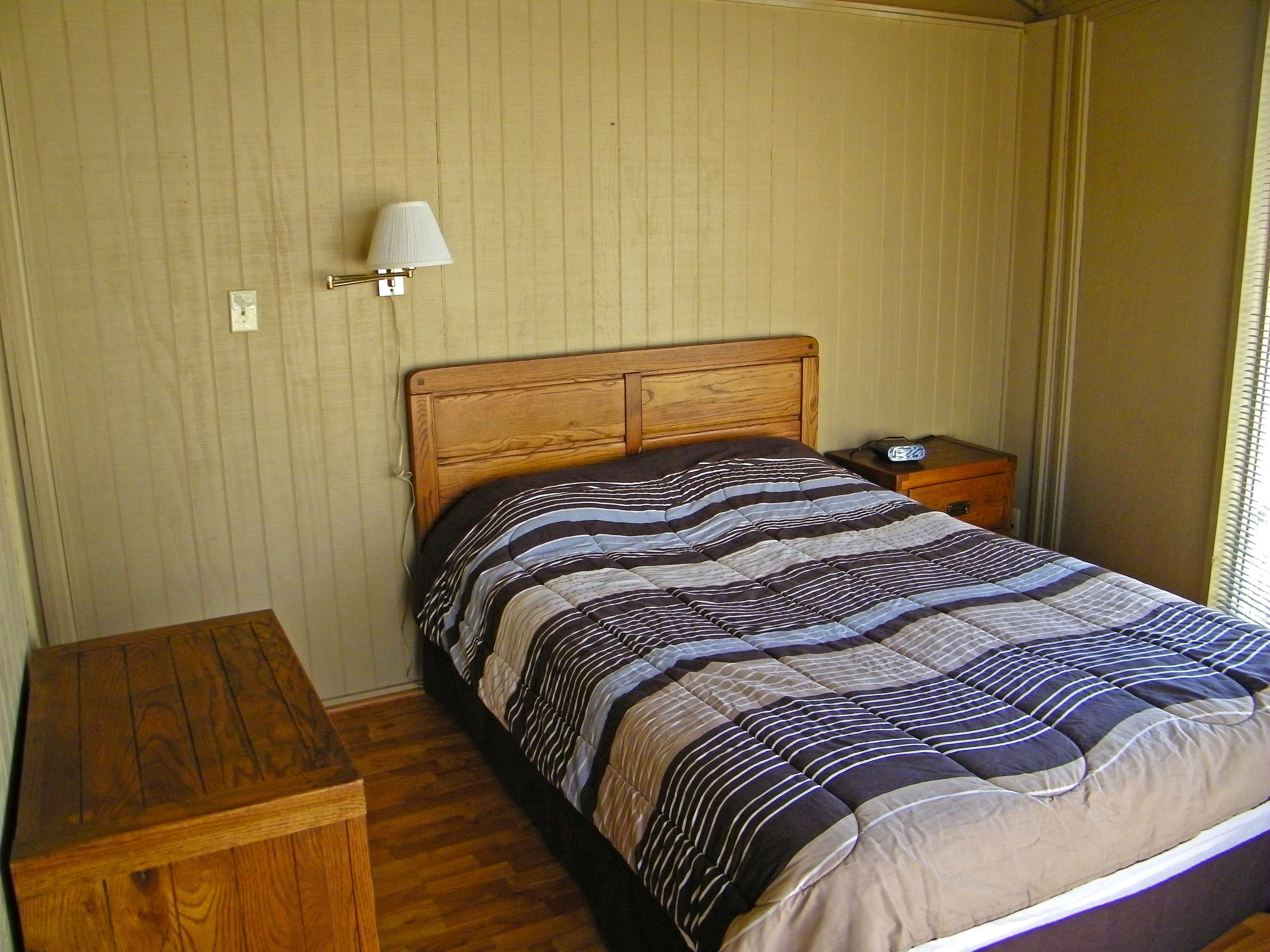 A bedroom with a wooden bed, a bedside table, a lamp, and a nightstand.
