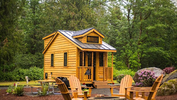 A wooden cabin with a porch, surrounded by greenery. - Mt Hood Village RV Resort (Welches)