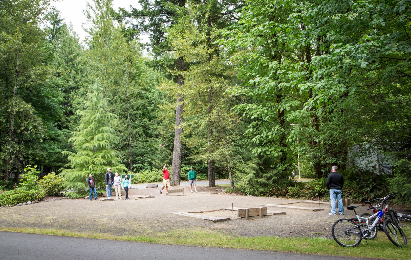 A park with a paved area, trees, and a bicycle parked by the roadside.