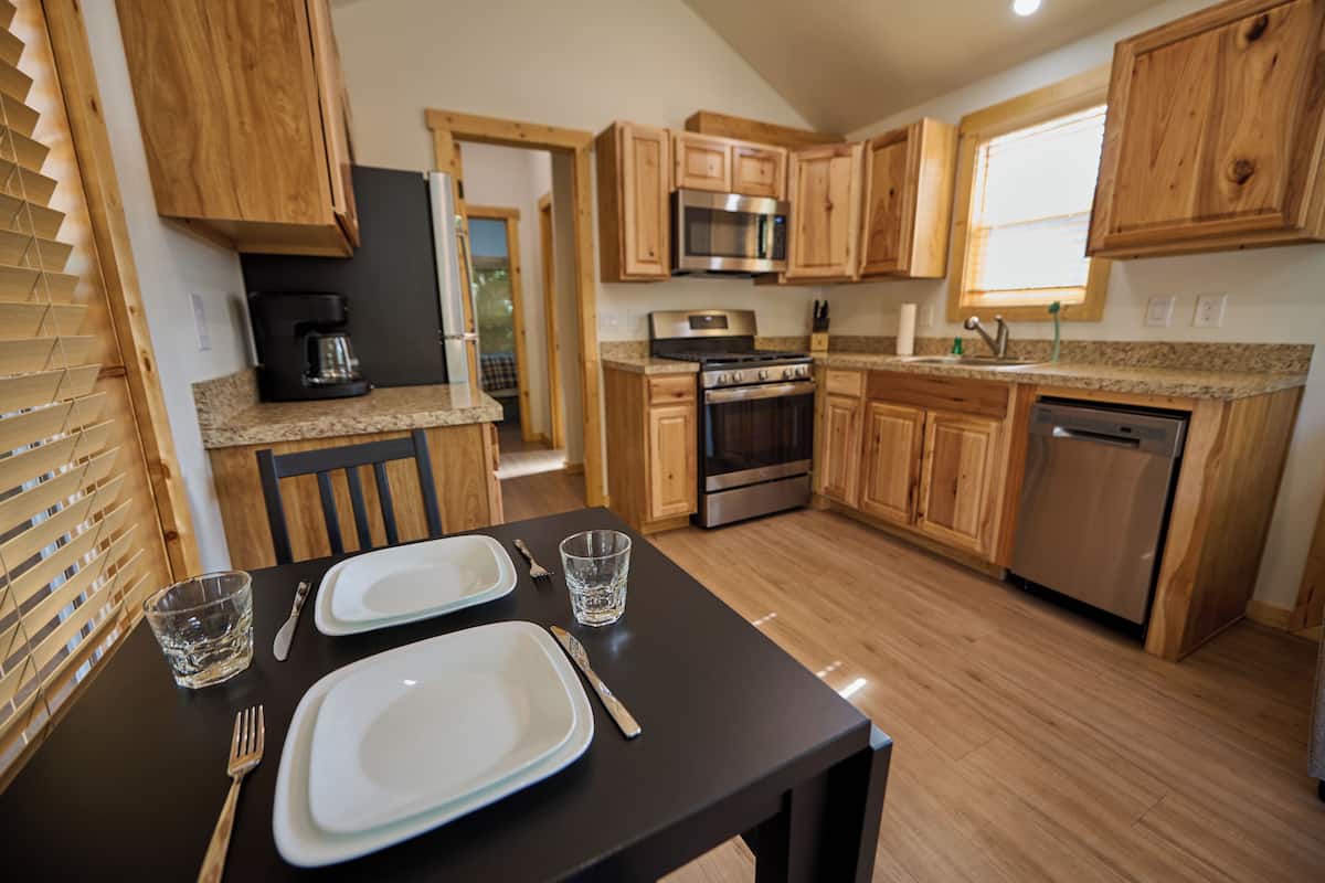 A modern kitchen with wooden cabinets, stainless steel appliances, and a dining area with a table set for two.