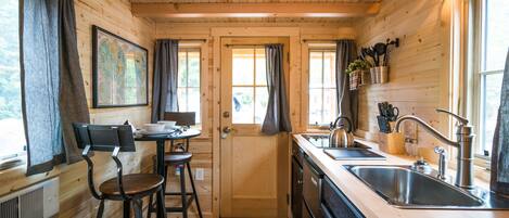 A wooden cabin kitchen with a wooden door, bar stools, a sink, and a stove.