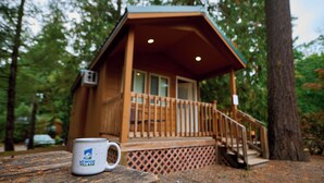 A cabin with a wooden deck and a small porch, surrounded by trees. - Mt Hood Village RV Resort (Welches)