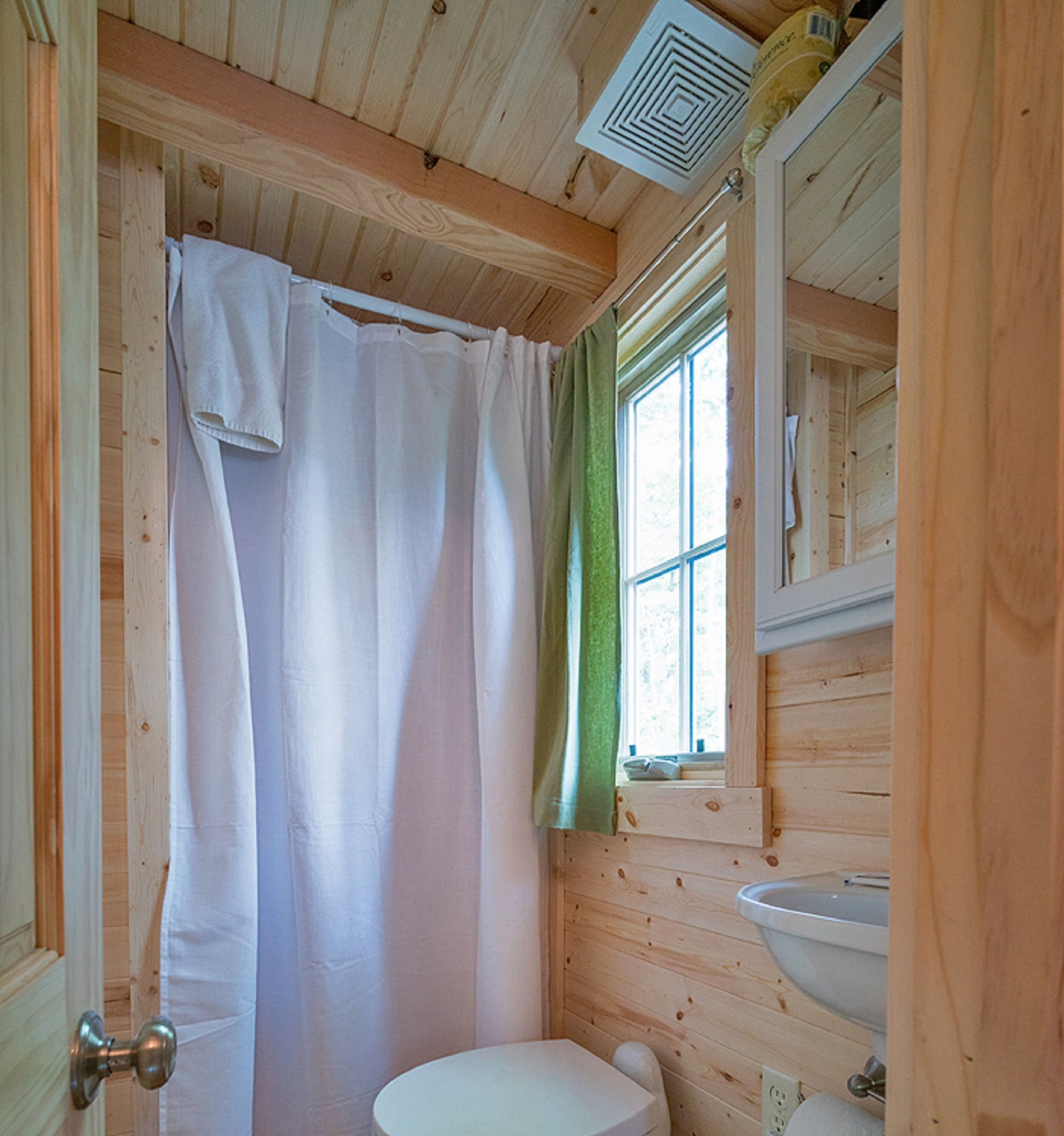 Un baño de cabaña de madera con un inodoro blanco, un lavabo y una cortina de ducha.