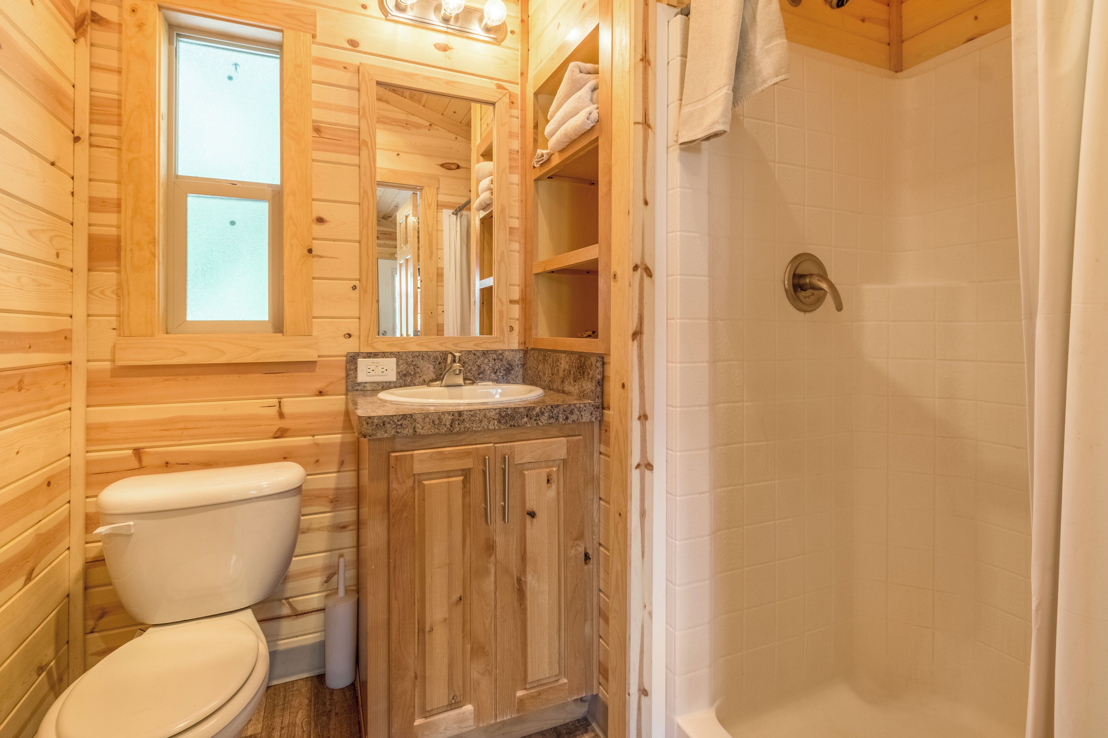 A wooden cabin bathroom with a toilet, sink, and shower.