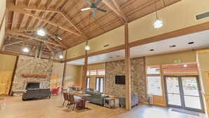 A spacious indoor area with a high ceiling, stone walls, a fireplace, and multiple seating arrangements. - Mt Hood Village RV Resort (Welches)