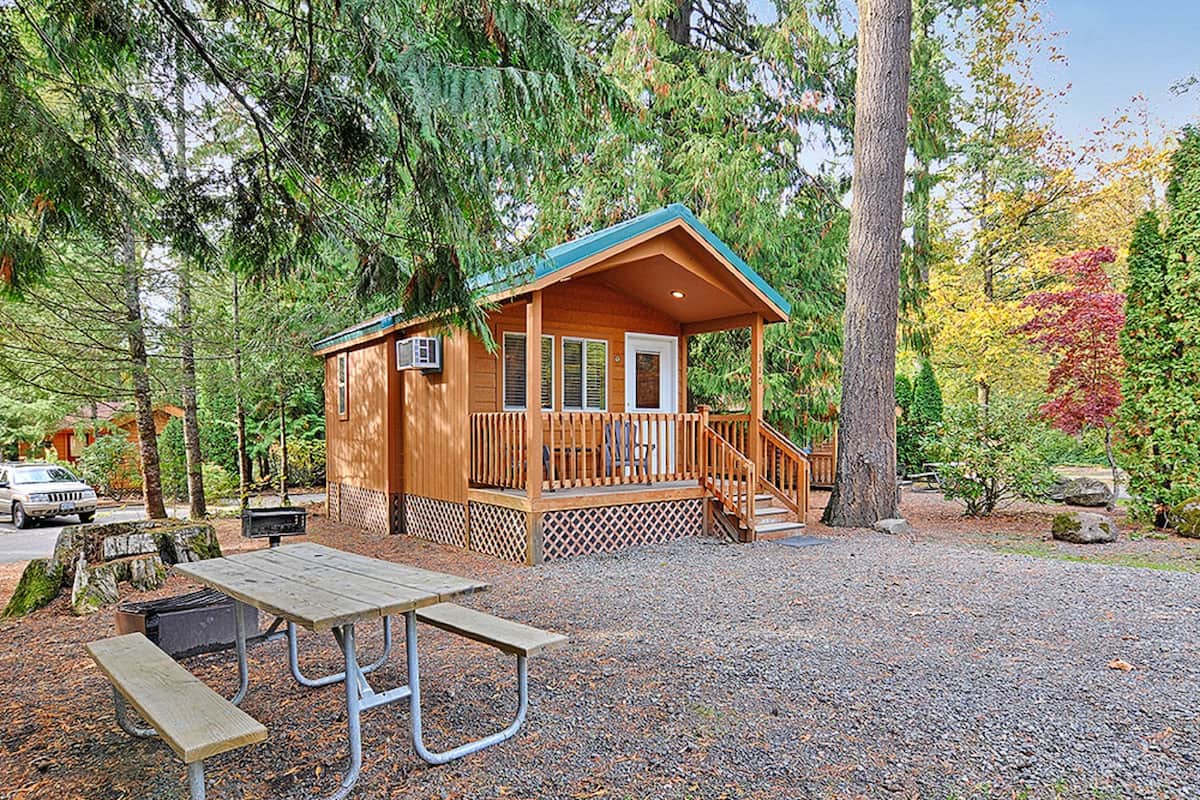 A wooden cabin with a porch, a picnic table, and a gravel ground.
