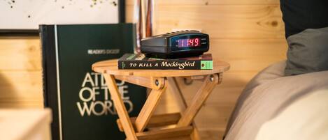 Ein Nachttisch mit einer digitalen Uhr, die 11:49 anzeigt, einem Buch mit dem Titel 'To Kill a Mockingbird' und einem Buch 'Atlas der Welt'.