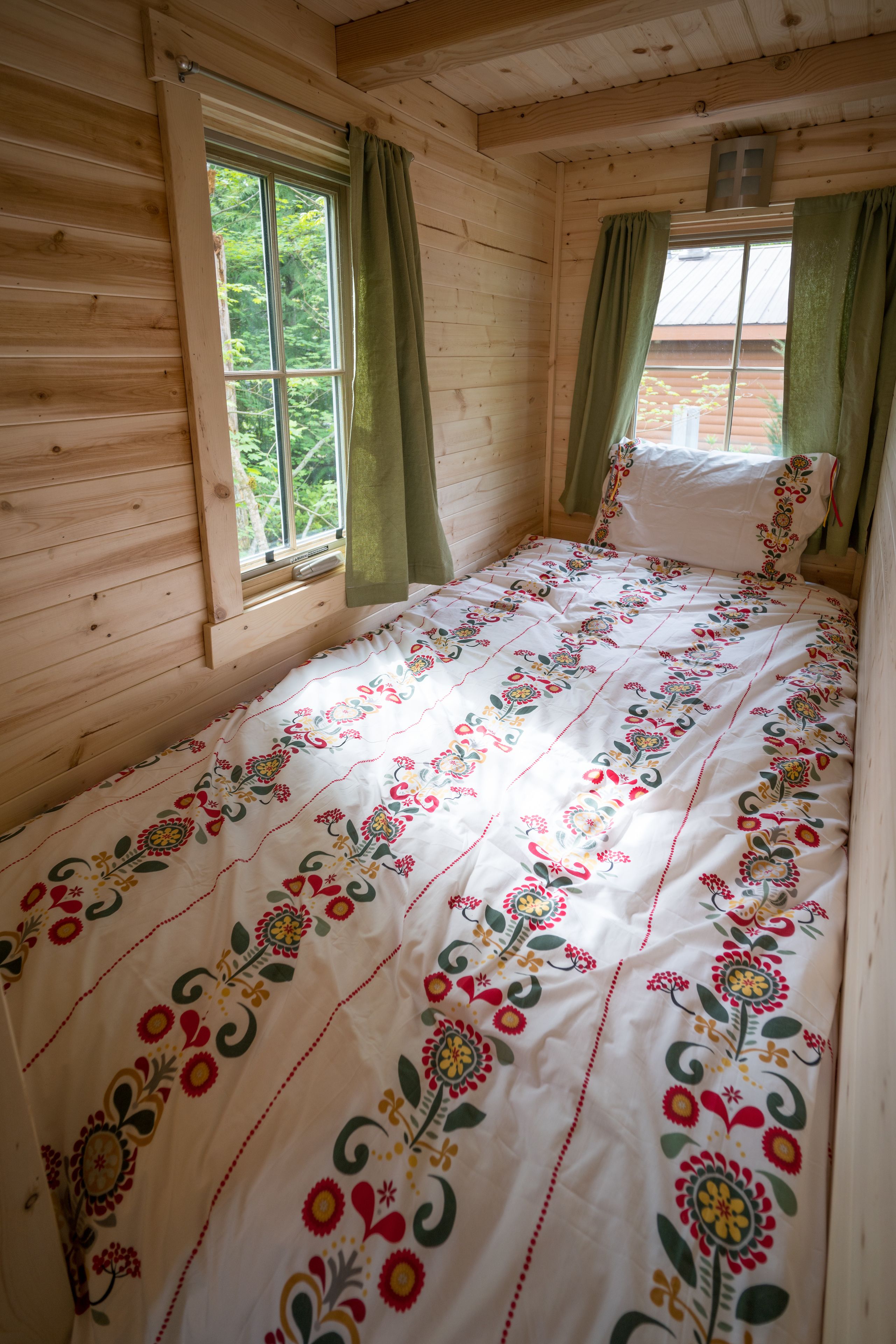 A wooden cabin bedroom with a bed, curtains, and a window.