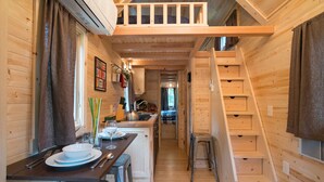 A compact wooden cabin interior with a dining area, kitchen, and a staircase leading to an upper level. - Mt Hood Village RV Resort (Welches)