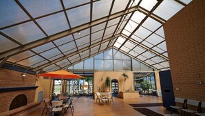 Un patio interior con paredes de ladrillo, techo de vidrio y chimenea. Mesas y sillas dispuestas para comer.