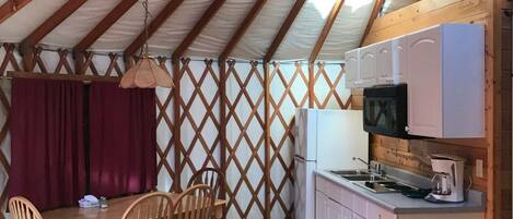 A tent with a wooden interior, a dining table with chairs, a kitchen area with a microwave, and a refrigerator.