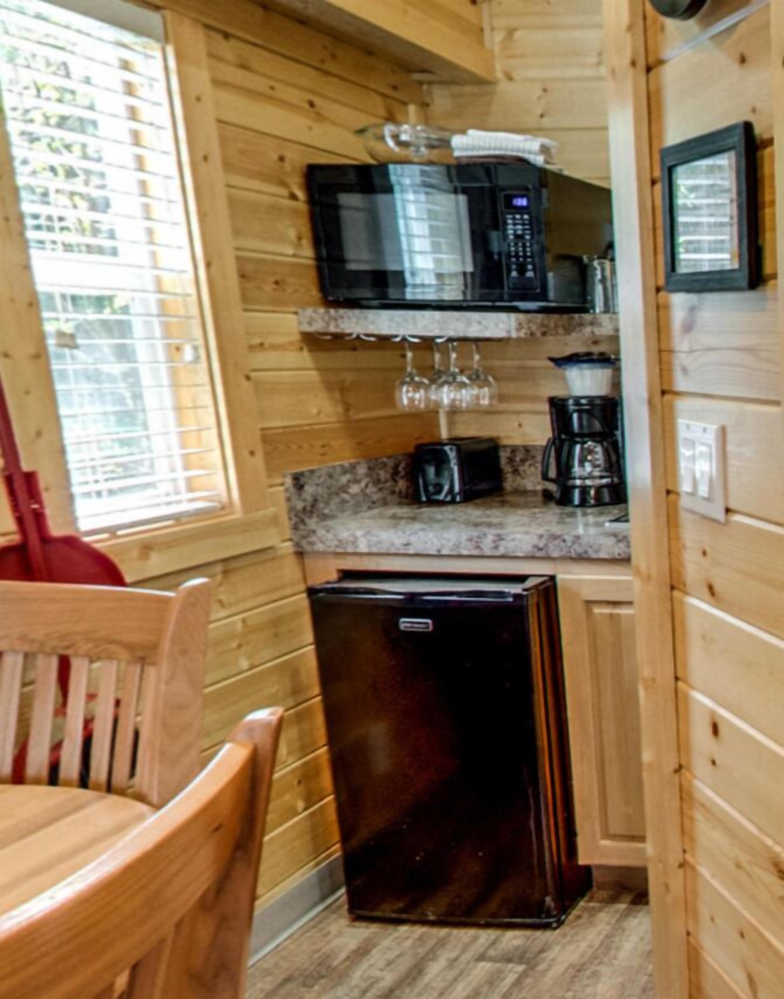 A compact kitchen with wooden walls, a microwave, a coffee maker, and a refrigerator.