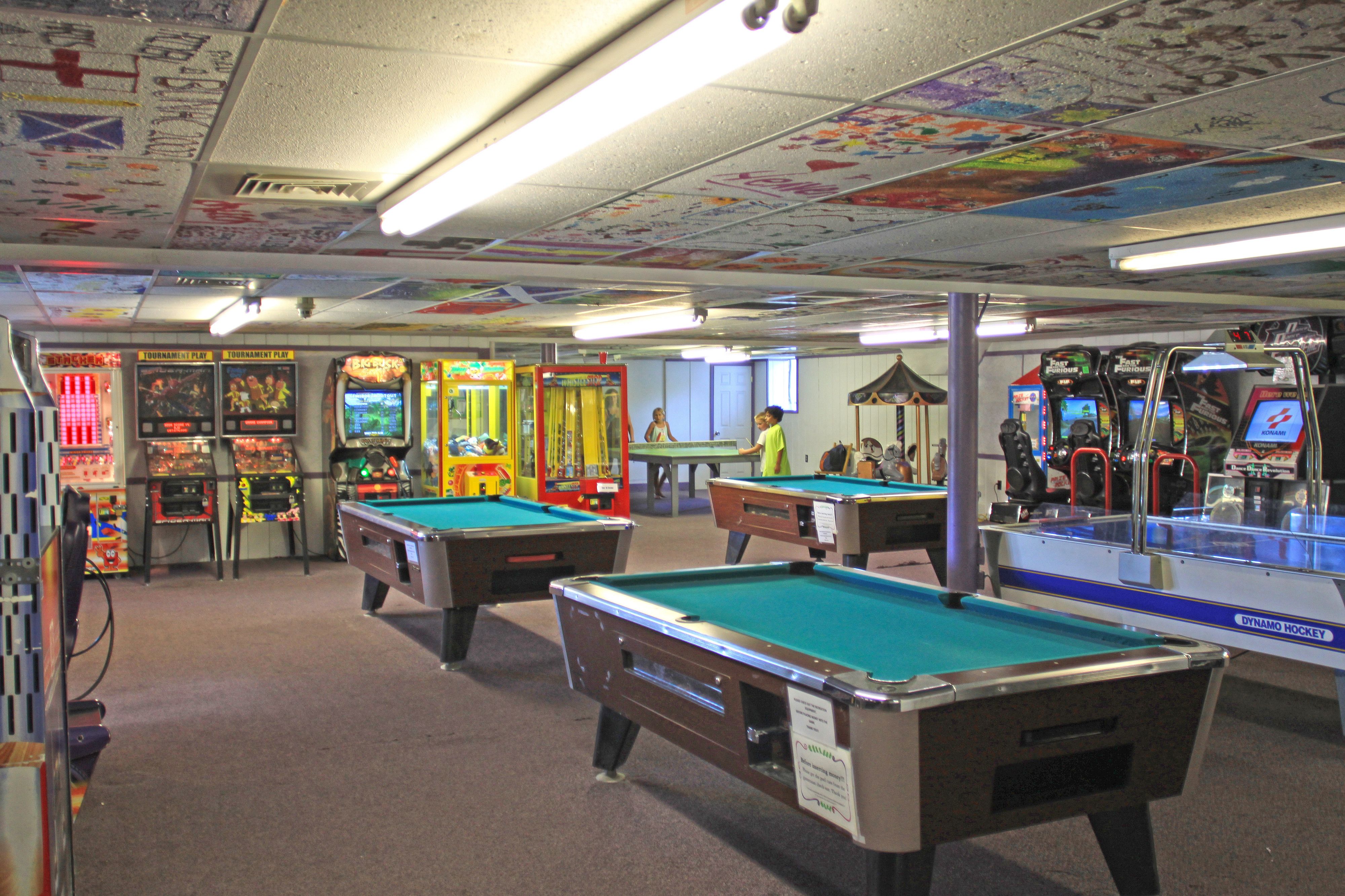 A pool hall with multiple pool tables, arcade games, and a ceiling with colorful murals.