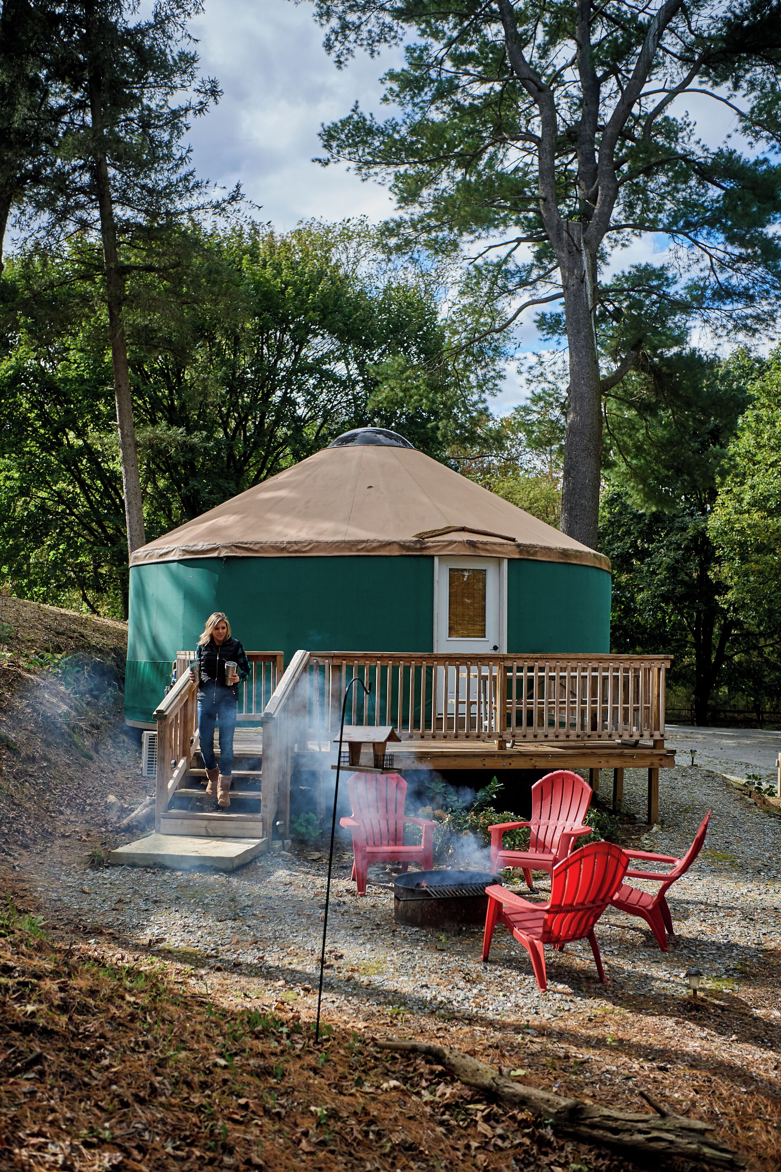 A yurt with a wooden deck and a fire pit, surrounded by trees.