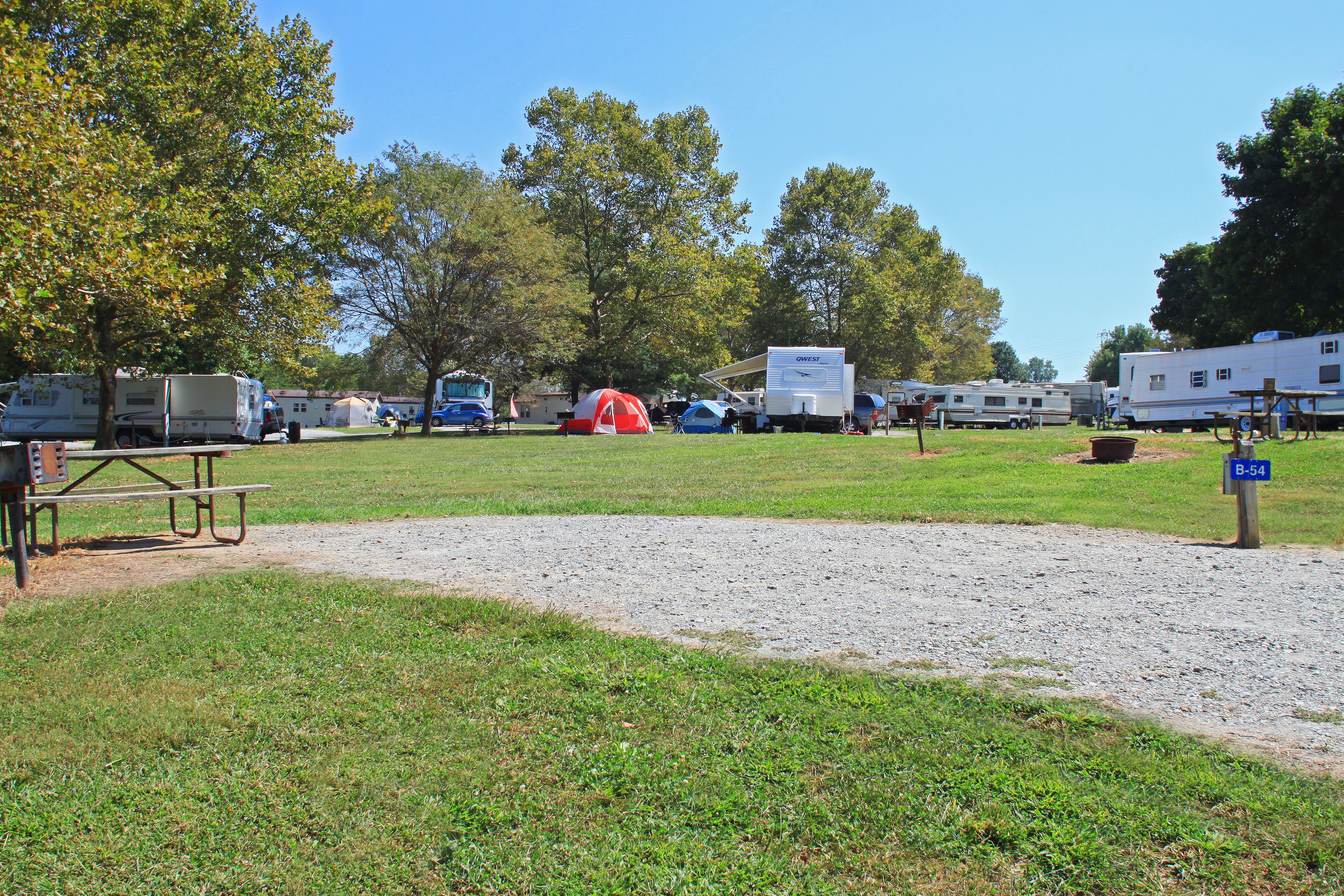 Un terrain de camping aménagé pour accueillir des camping-cars et des tentes, avec des tables de pique-nique et un sentier de gravier.