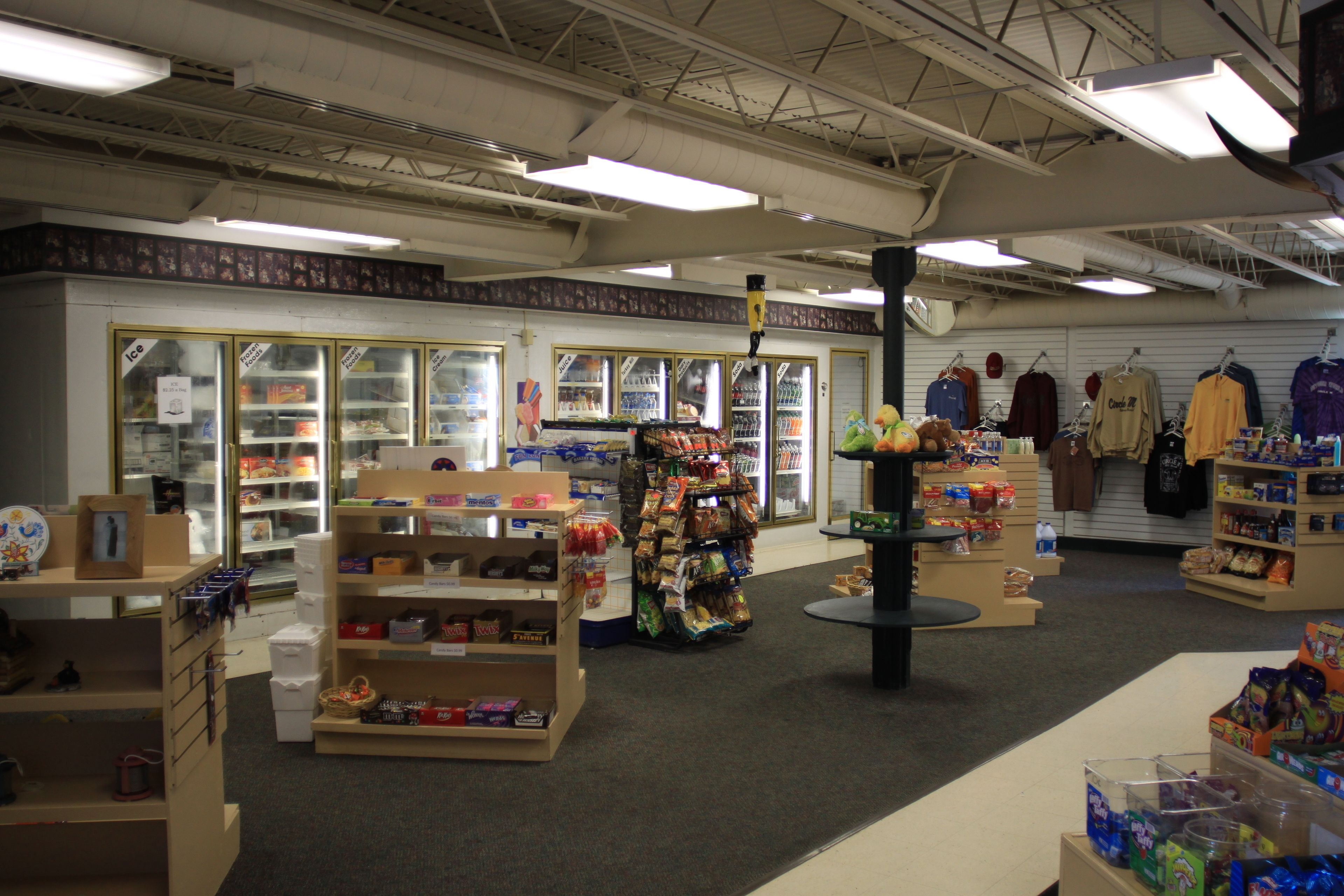 A retail store with shelves stocked with various products, a refrigerated display case, and a section with hanging clothes.